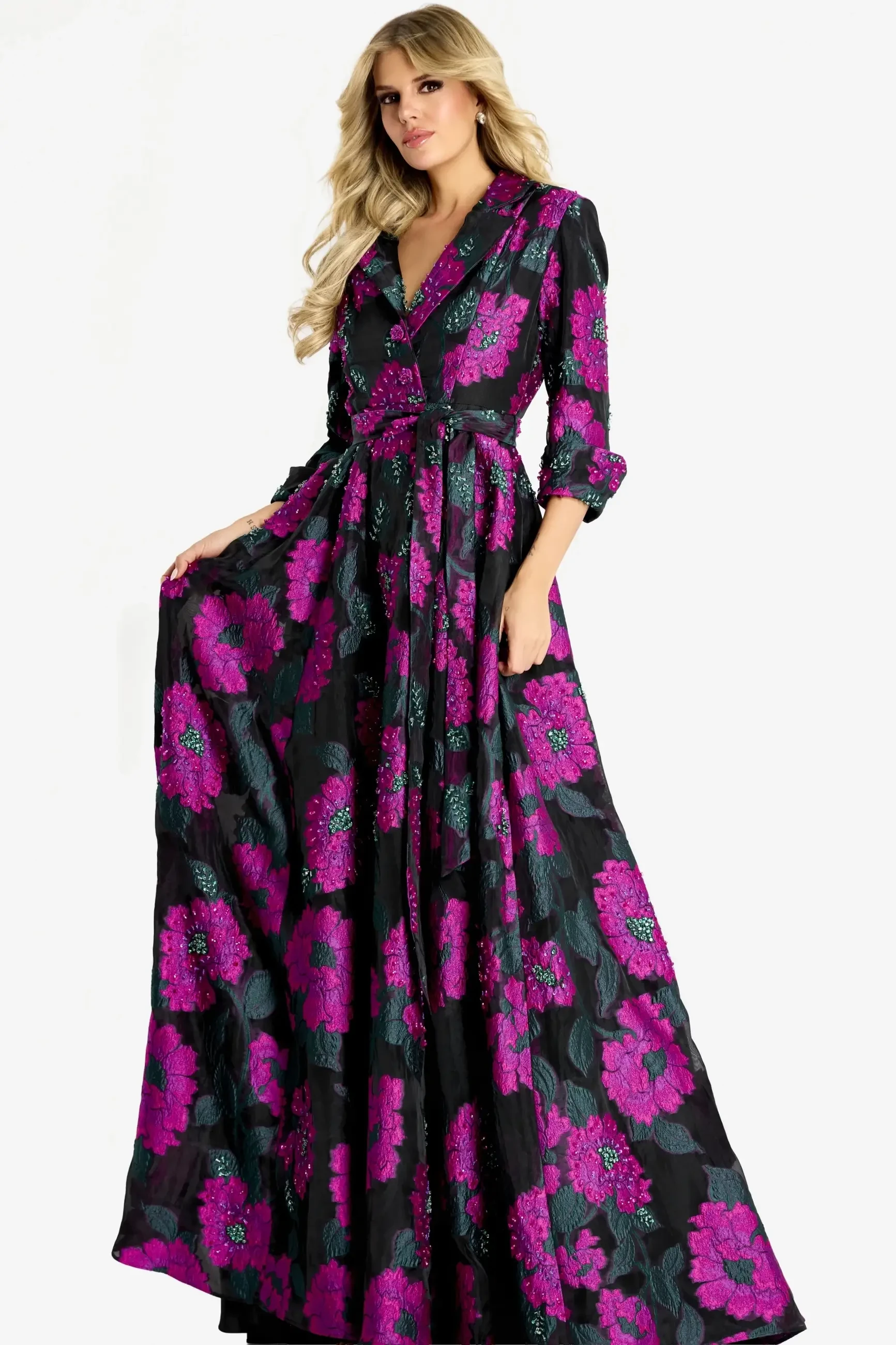 A woman wearing a long, floral dress with large pink and purple flowers on a black background, posing gracefully.