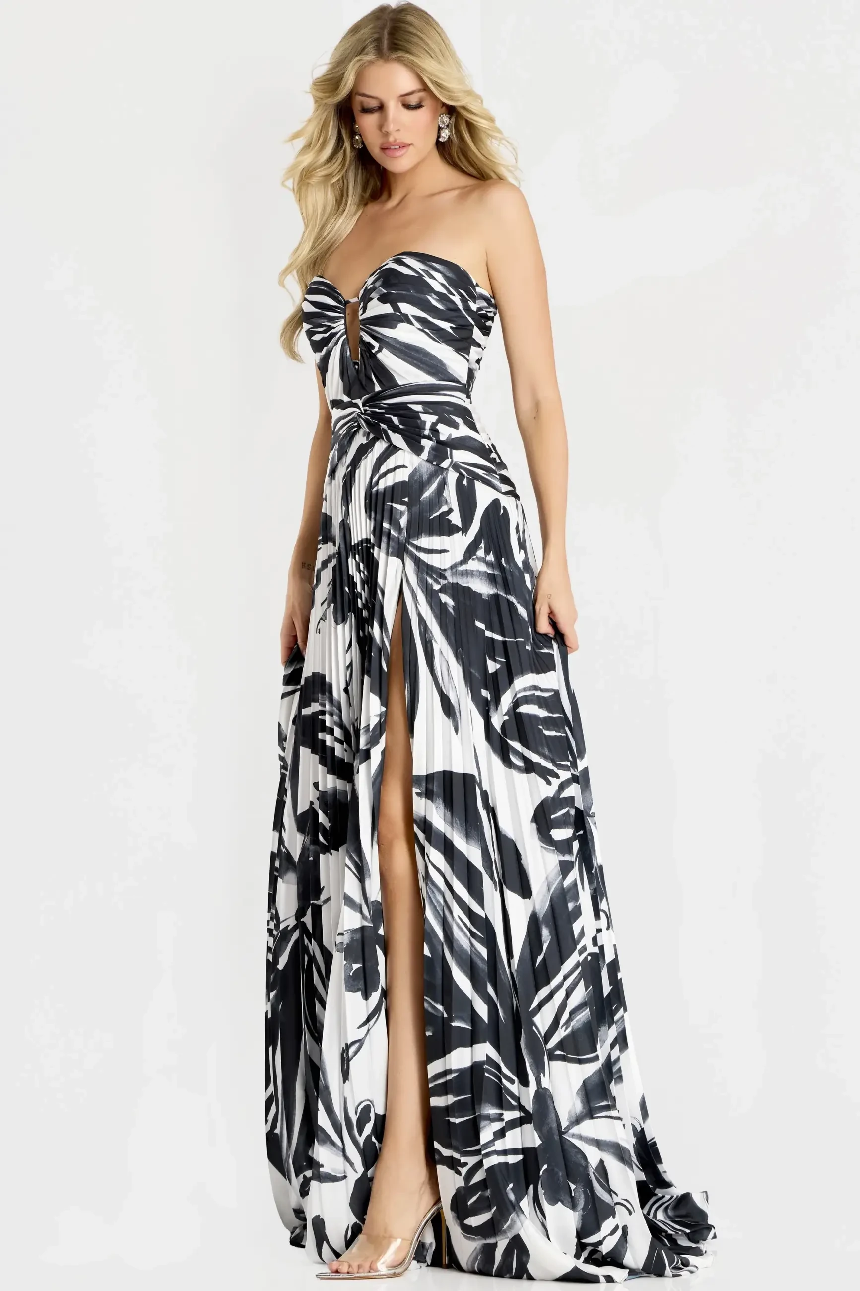 A woman wearing a strapless, long dress with a floral pattern, featuring a high slit on one side. She has long blonde hair and is standing in a neutral pose.